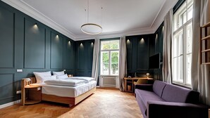 A bedroom with a bed, a purple sofa, a desk, and a TV. - Hotel Uhland (Munich)