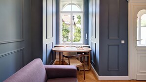 A narrow hallway with a dining table and chairs, a purple bench, and a white door with a window. - Hotel Uhland (Munich)
