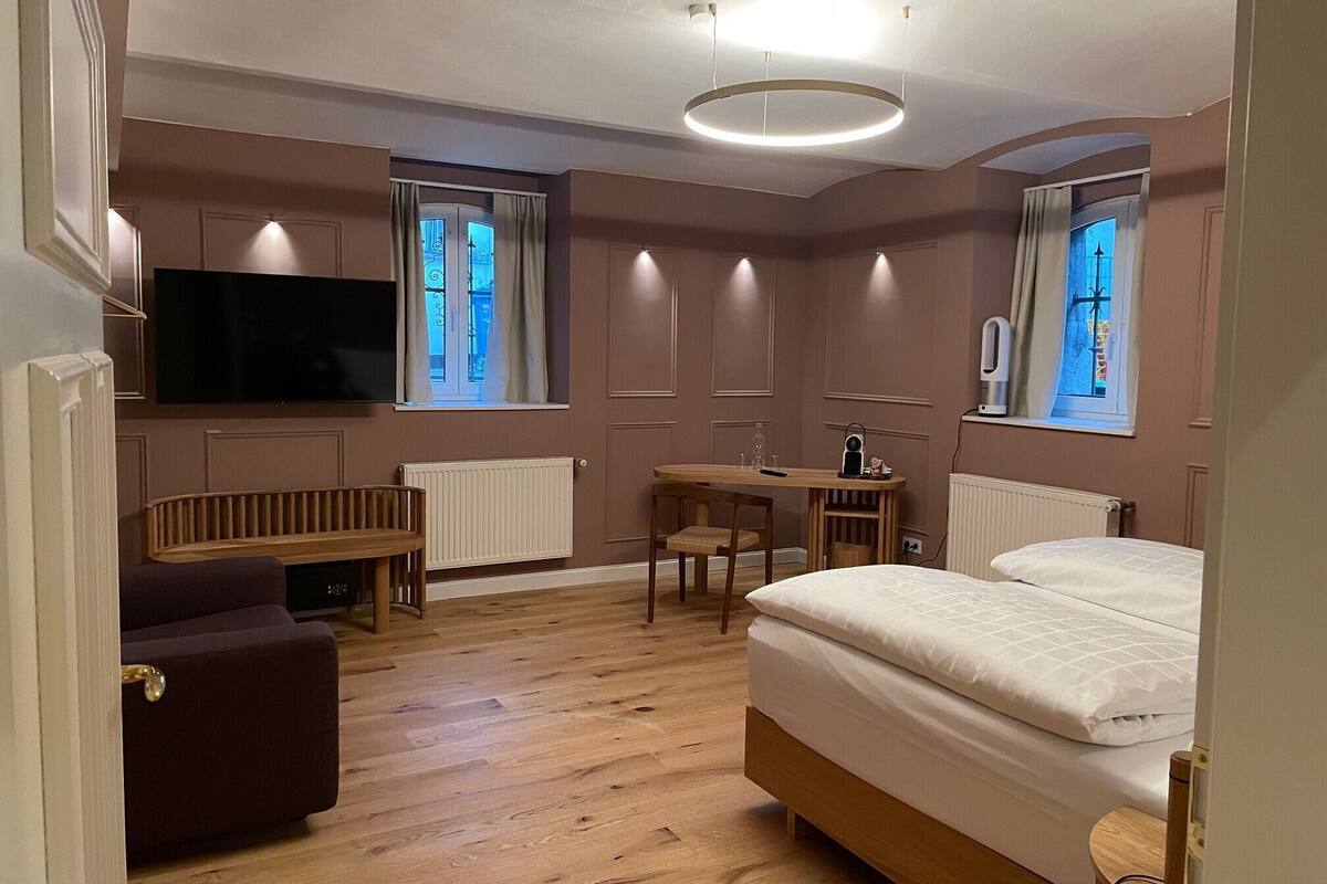 A modern bedroom with a bed, a desk, a chair, a TV, and two windows.