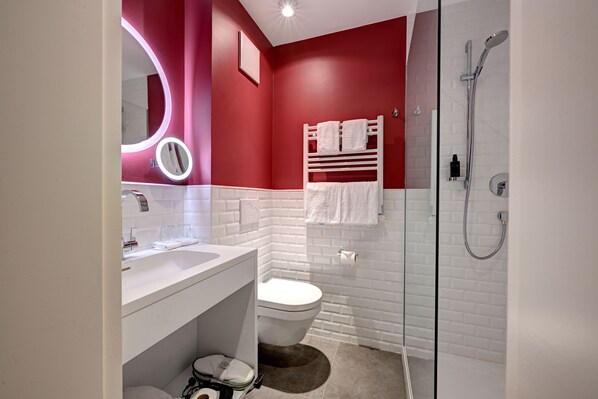 Un baño moderno con una pared de acento roja, un lavamanos blanco, un box de ducha de vidrio y un perchero blanco.