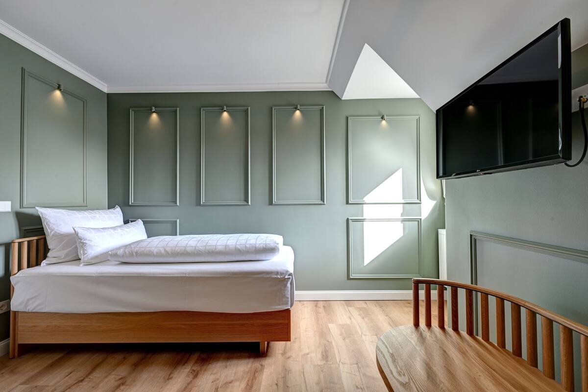 A bedroom with a wooden bed, a flat-screen TV mounted on the wall, and a skylight.