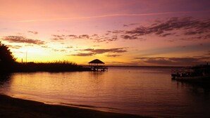 Un atardecer sobre aguas tranquilas con un muelle de madera y una estructura con techo de paja.