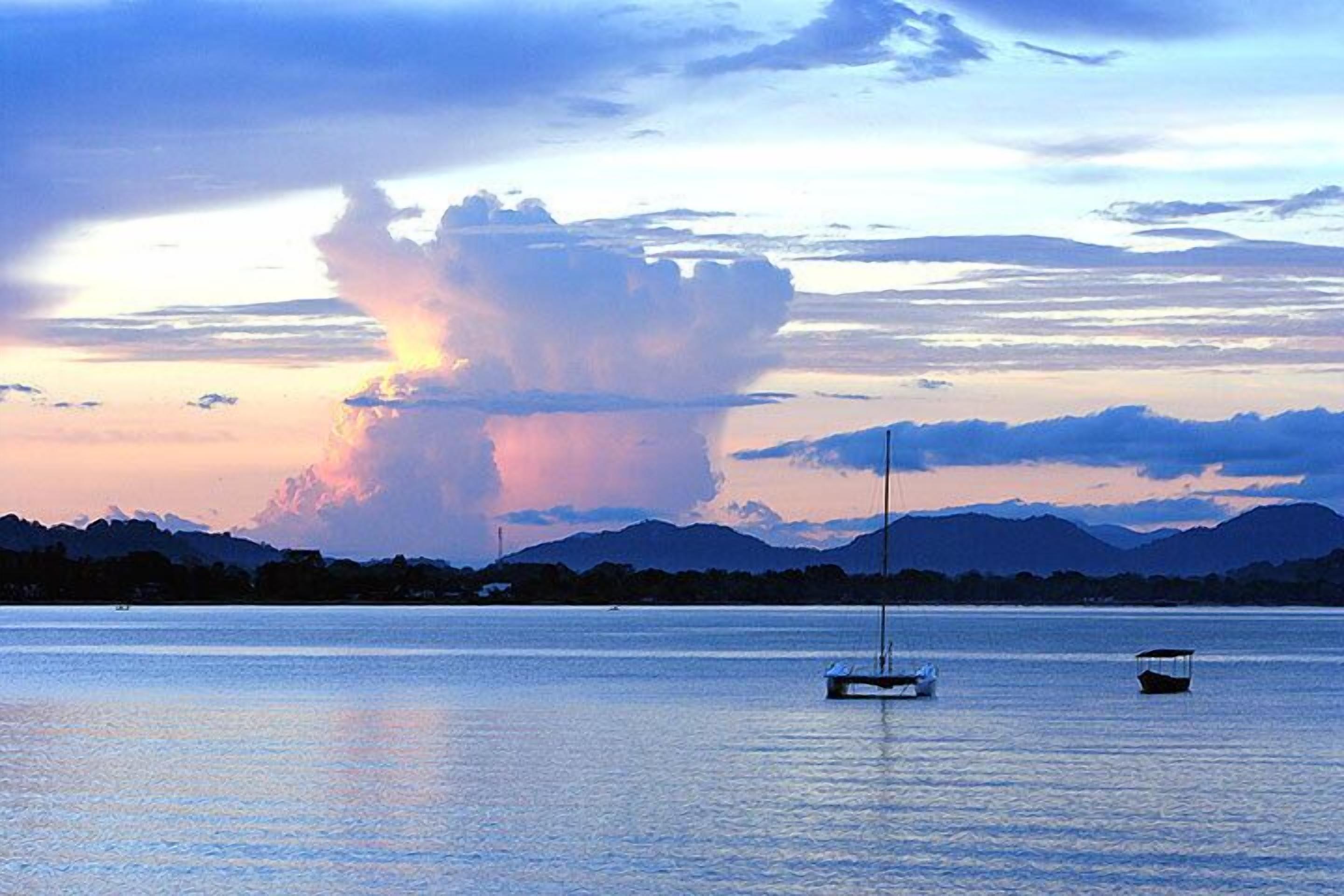 A calm lake with boats, mountains in the background, and a sunset sky.