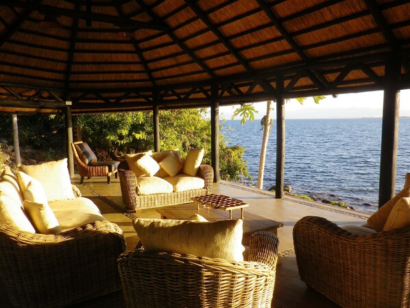 Un espacio de estar al aire libre cubierto, con mobiliario de mimbre y vista al mar.