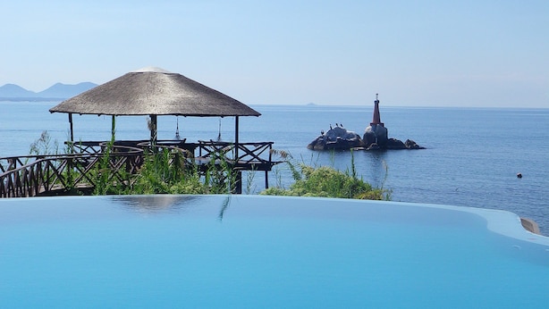 Una piscina infinita con una estructura de techo de paja y un faro al fondo.