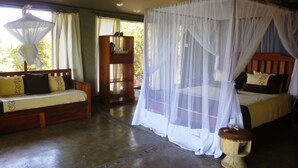 Una habitación con una cama bajo un dosel, un sofá con cojines, un armario de madera y un taburete pequeño.