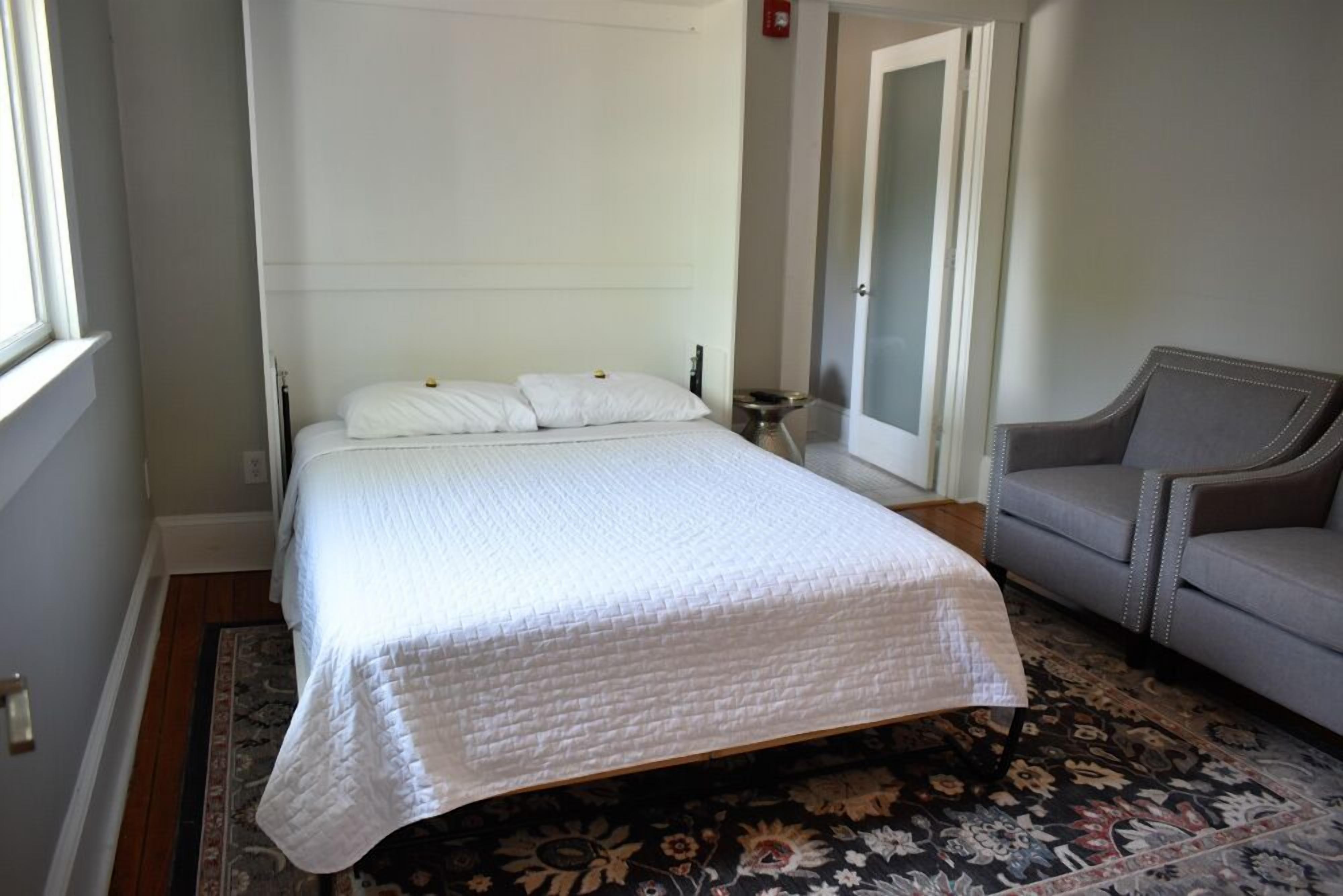 A neatly arranged bedroom with a bed, a chair, a nightstand, and a door.