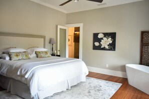 A bedroom with a bed, a nightstand, a lamp, a painting, and a bathtub.
