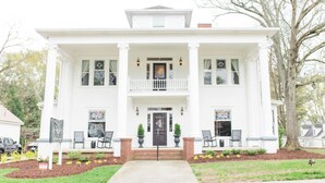 A two-story white house with a front porch, a balcony on the second floor, and a front door with a decorative glass panel. - Sparrow Grove Manor (Monroe)