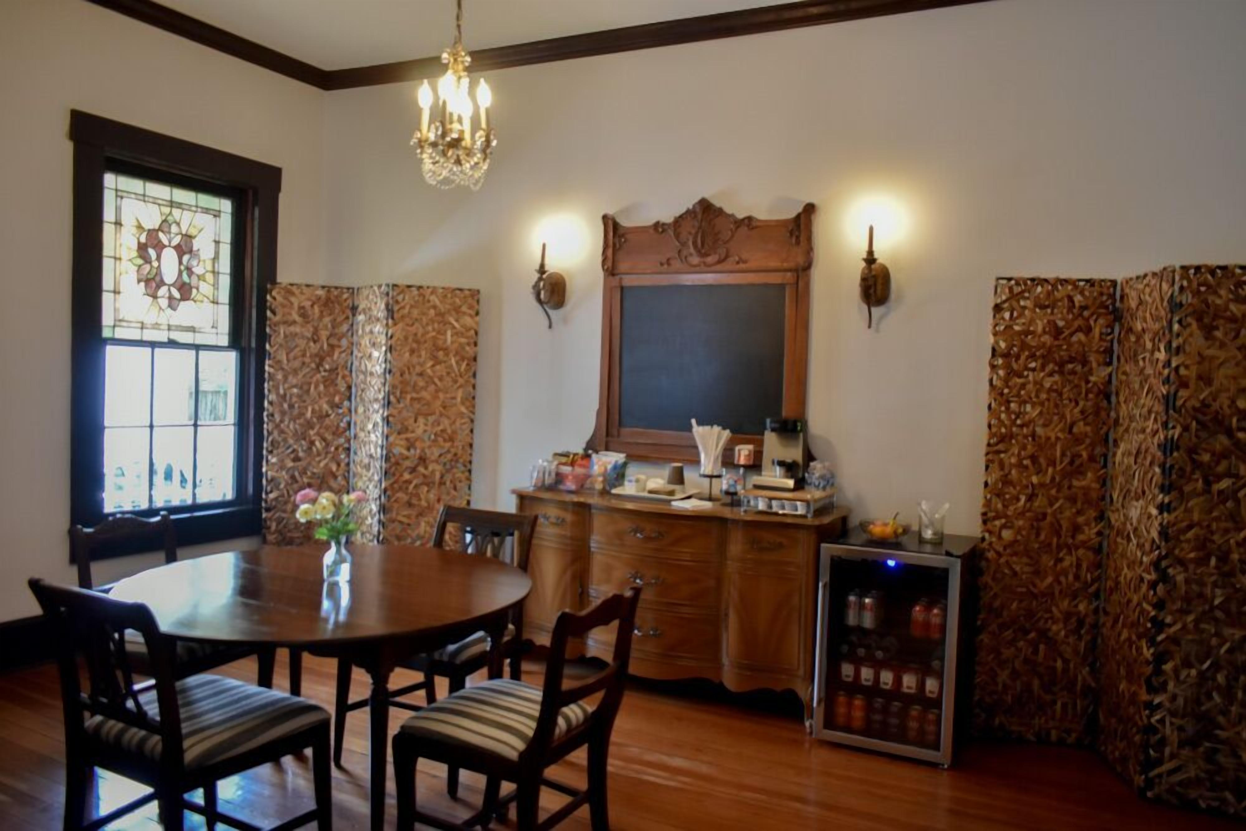 A dining area with a wooden table and chairs, a chandelier, a stained glass window, a wooden cabinet with a mirror, and a wall-mounted light fixture.