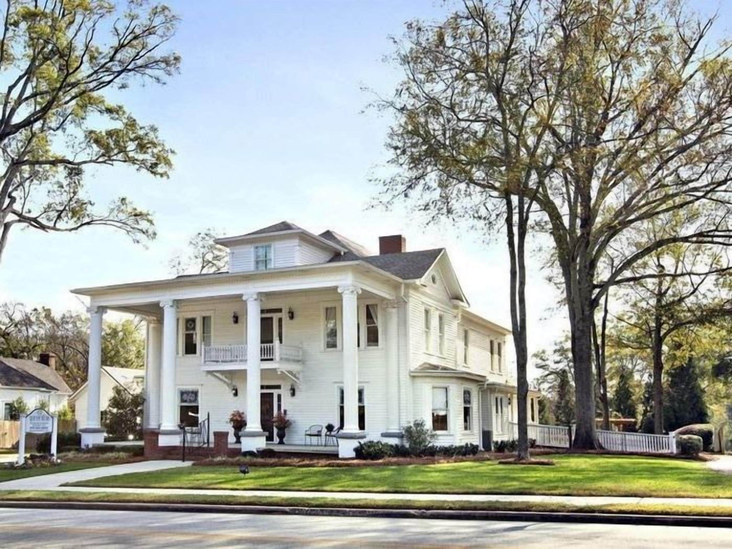 A two-story white house with a front porch, columns, and a small balcony.