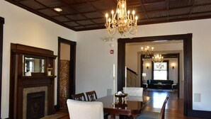 A dining area with a wooden table, chairs, and a chandelier. There is a fireplace on the left and a staircase leading to another room. - Sparrow Grove Manor (Monroe)