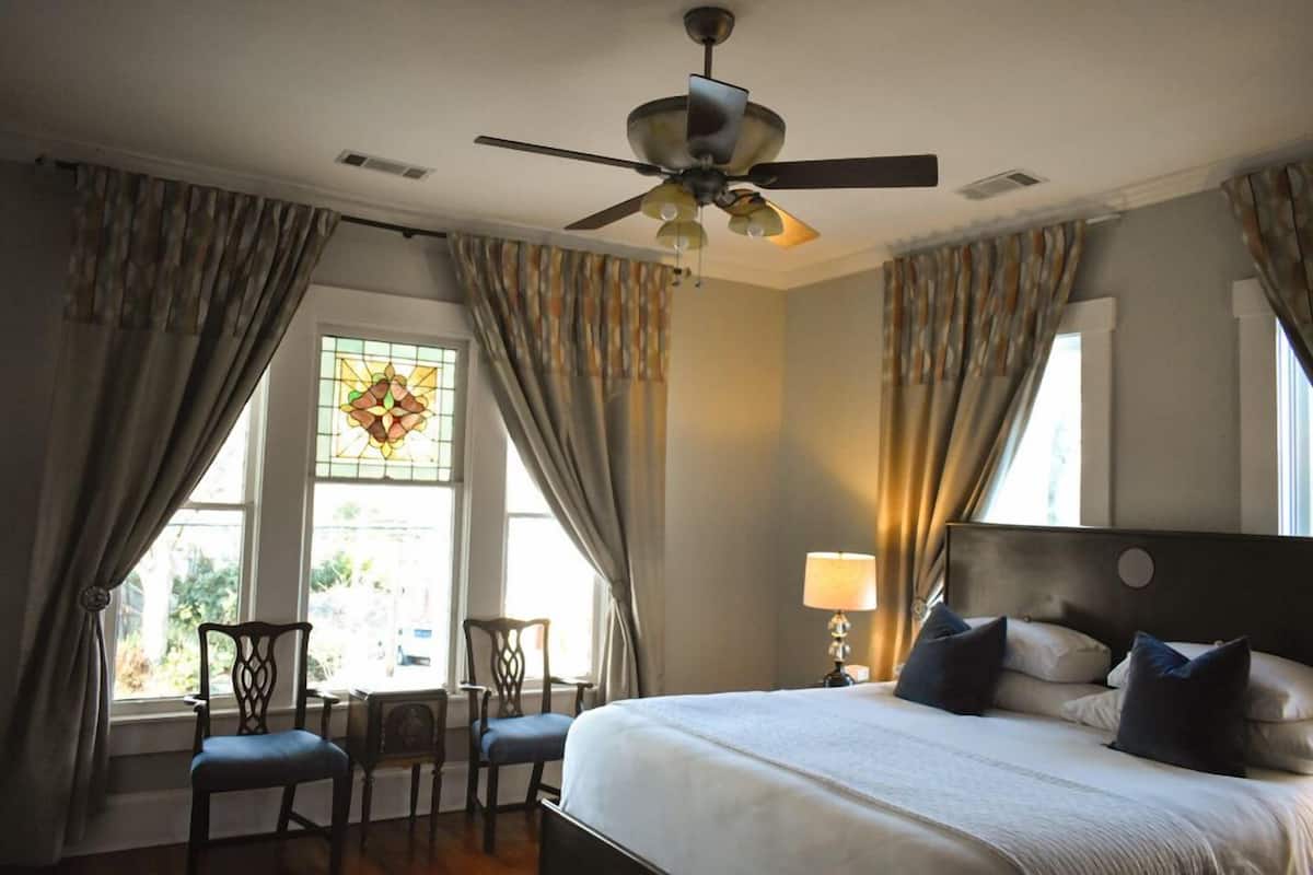 A hotel room with a bed, a ceiling fan, a window with curtains, and a chair.