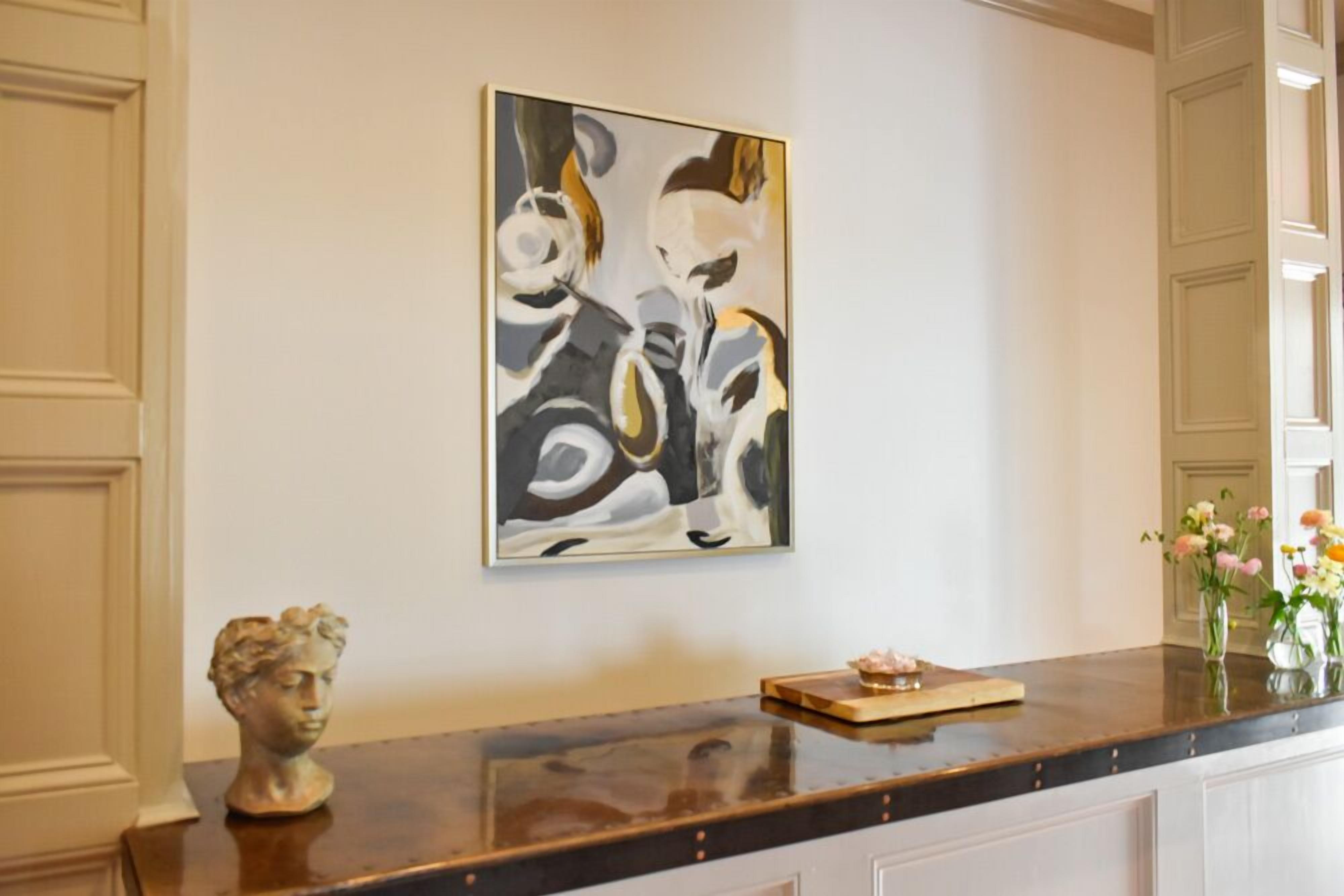 A reception area with a marble counter, a bust sculpture, a framed abstract painting, and a vase with flowers.