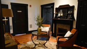 A room with a wooden floor, a leather chair, a glass table with a vase, a fireplace, and a door labeled "OFFICE". - Sparrow Grove Manor (Monroe)