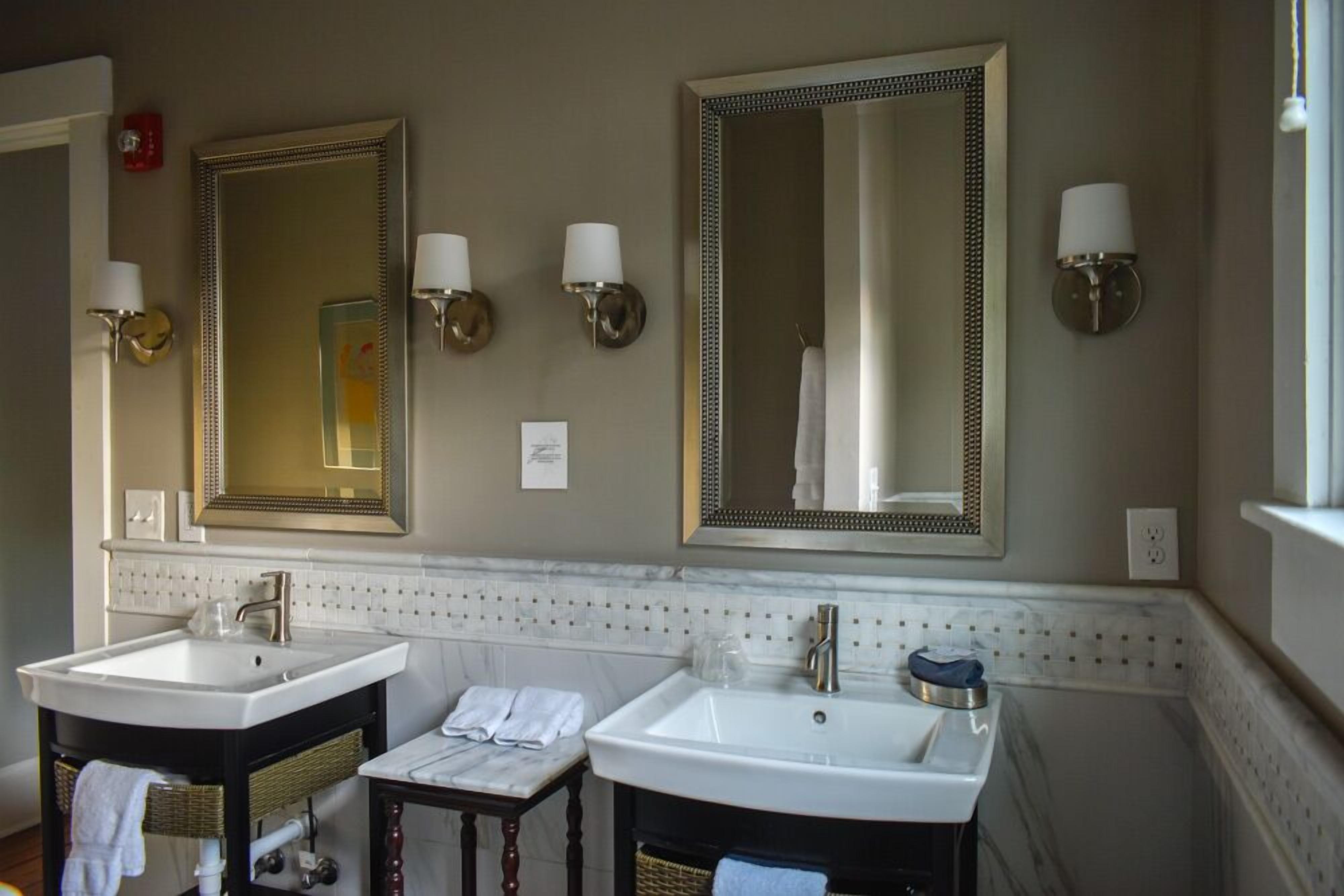 A bathroom with two sinks, a mirror, and wall sconces.