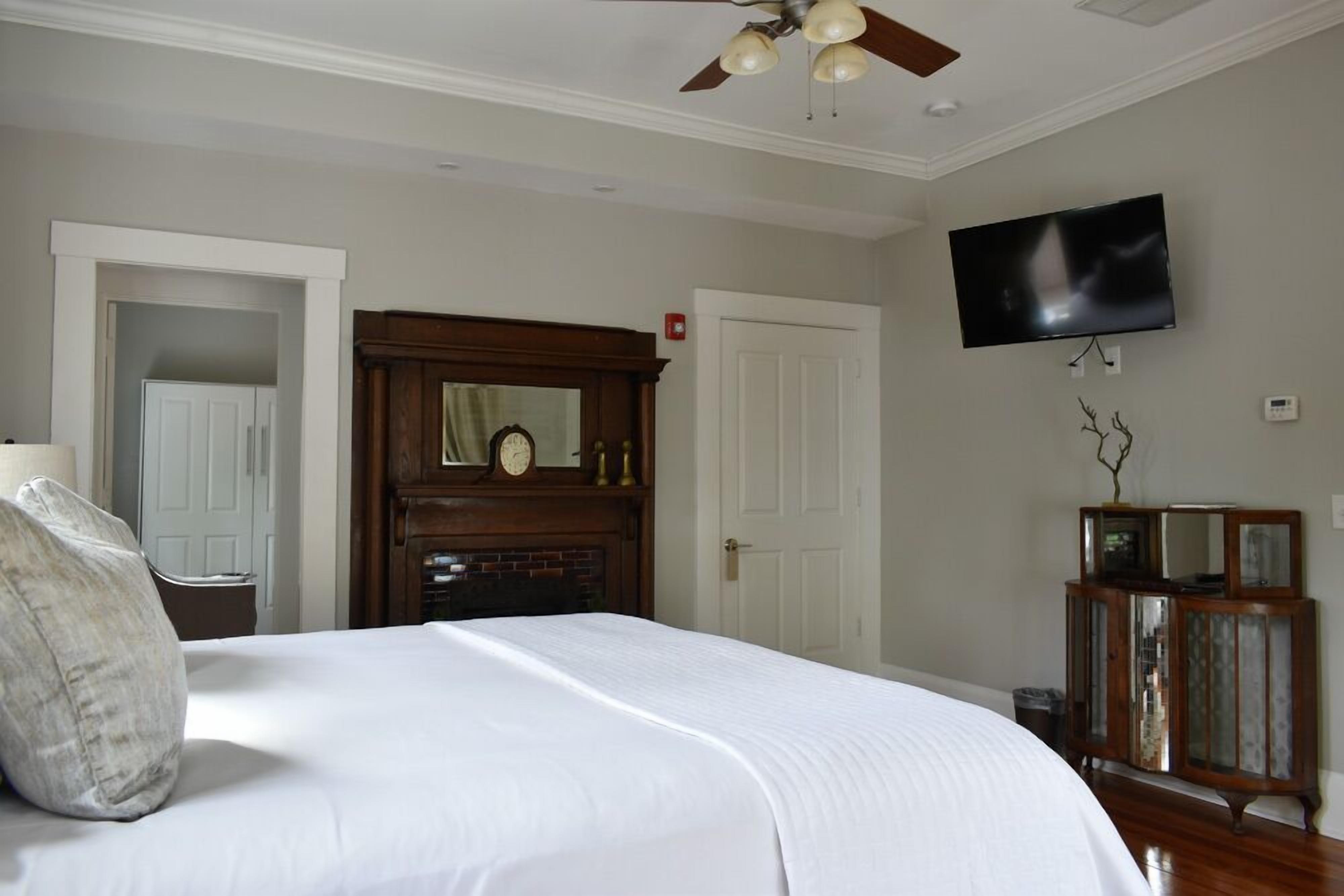 Un dormitorio con una cama grande, ventilador de techo, televisor montado en la pared y un armario de madera.