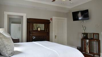 Un dormitorio con una cama grande, ventilador de techo, televisor montado en la pared y un armario de madera.