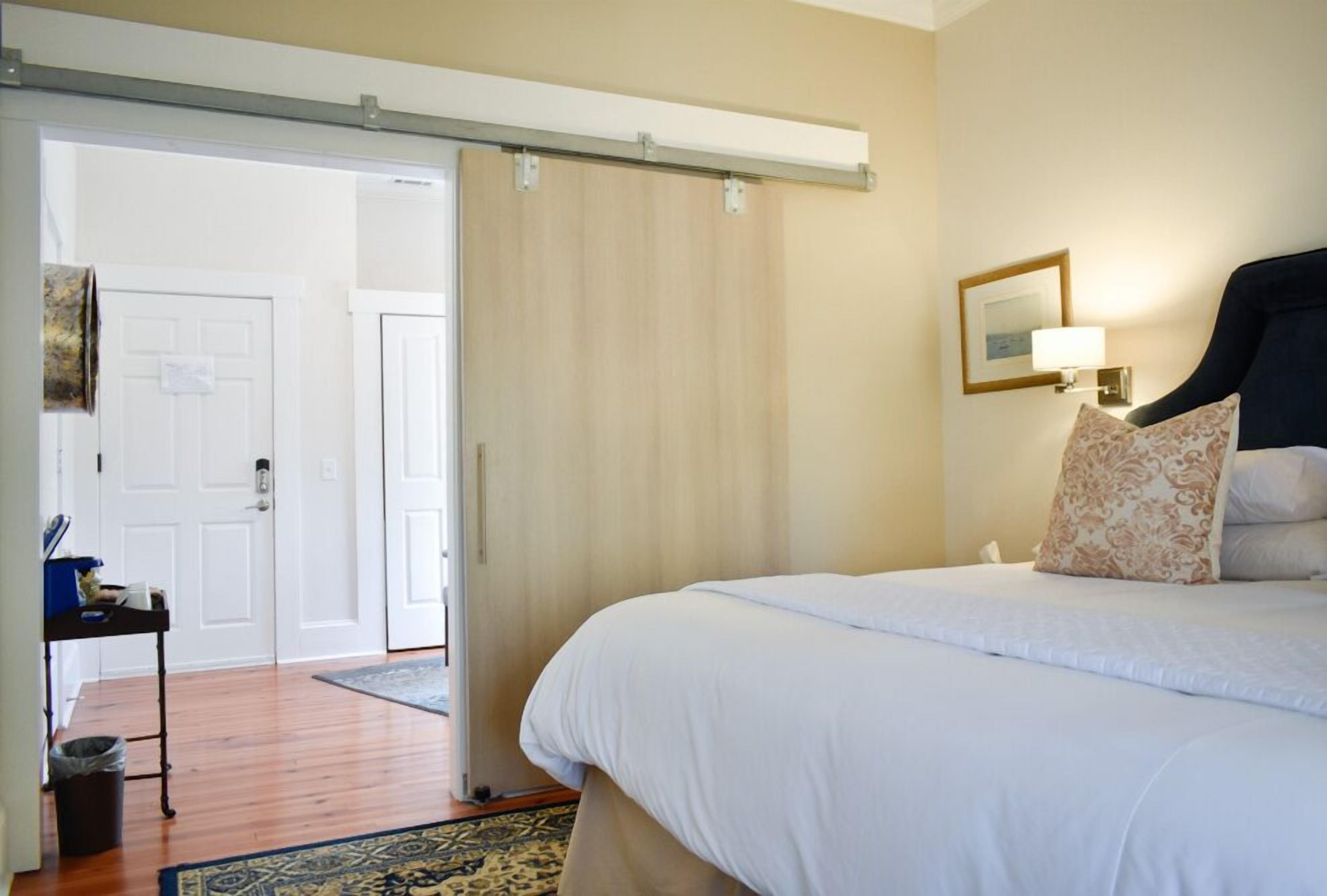 Een slaapkamer met een bed, nachtkastje, lamp en een schuifdeur naar een andere kamer.