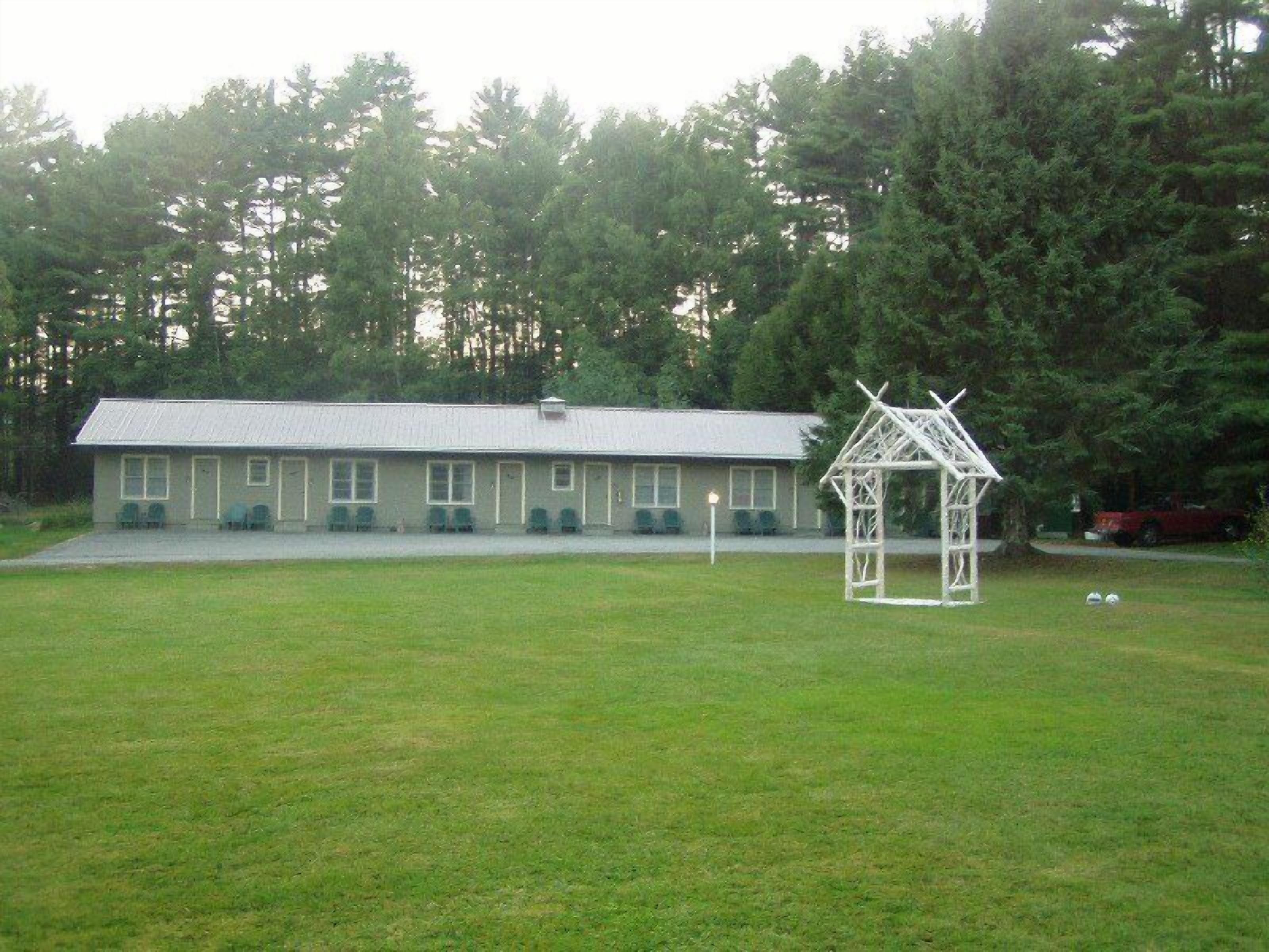 A building with a simple, functional design, a covered outdoor seating area, and a lawn in front.