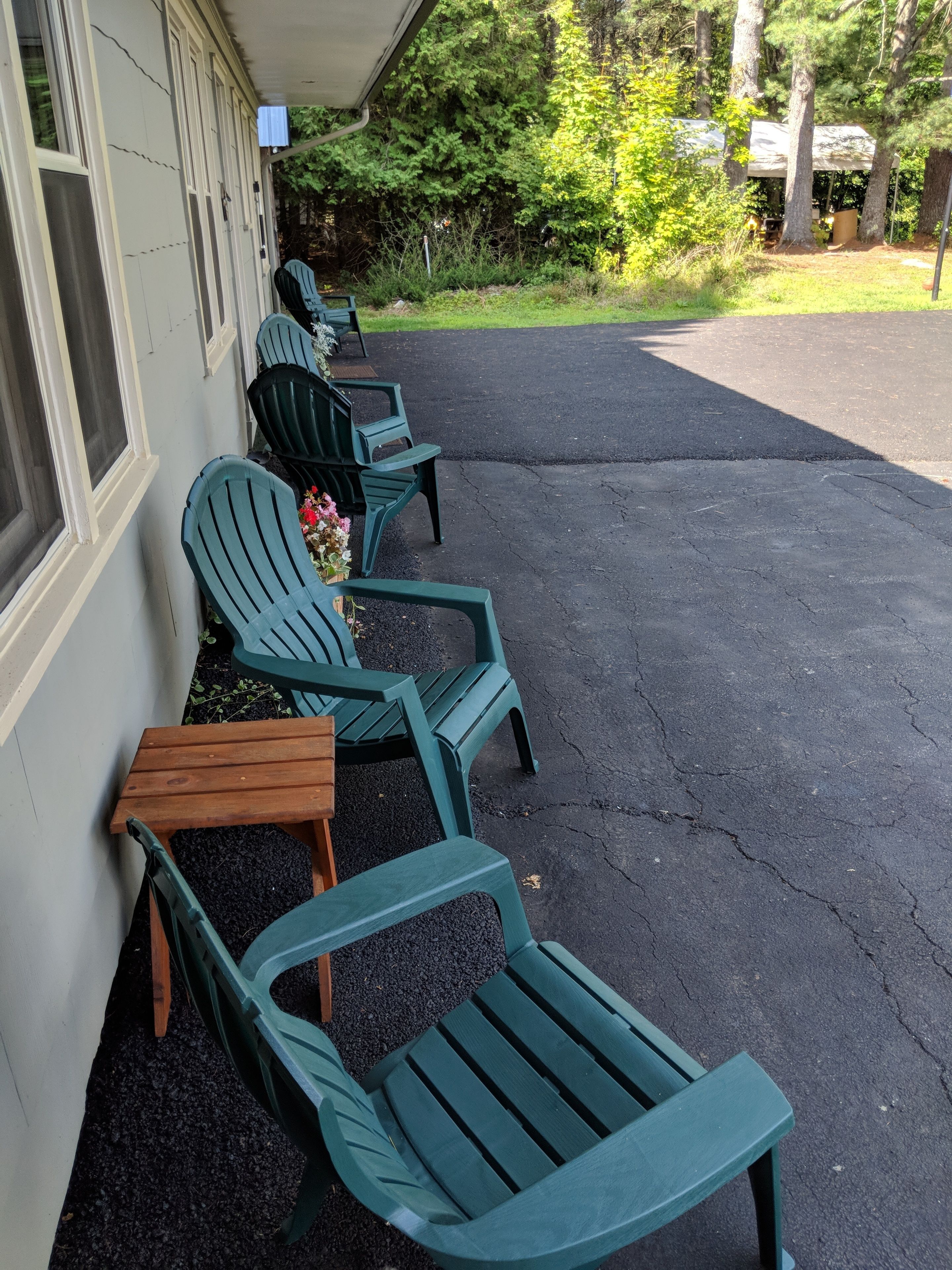 Terrasse mit Stühlen und Tisch, ein Gebäude mit Fenstern und ein gepflasterter Zugangsbereich.