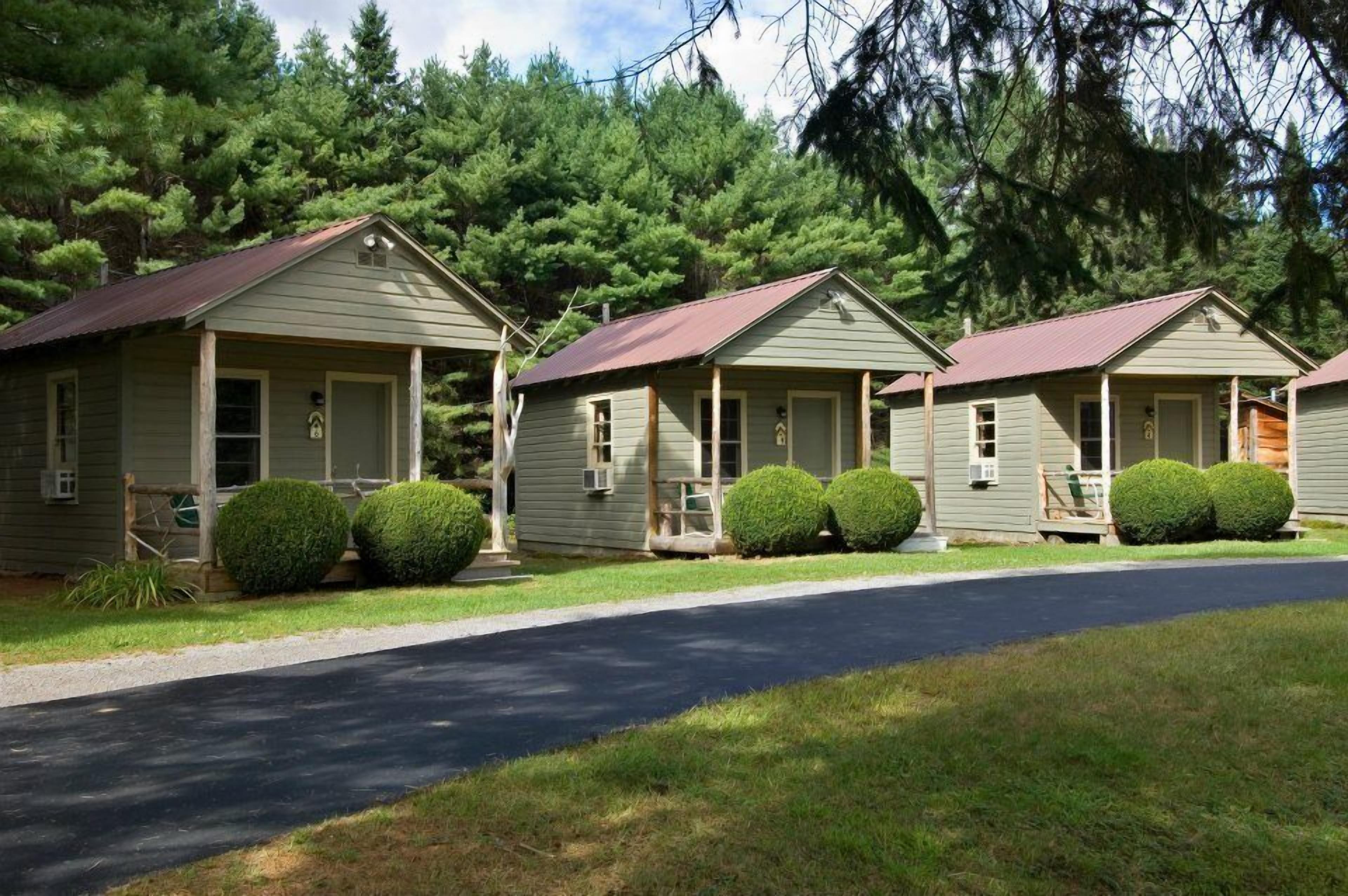 A row of small, single-story cabins with a peaked roof, surrounded by well-maintained lawns and dense forest.