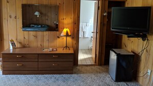 Una habitació amb parets de fusta, un llit, una petita còmoda, una televisió i un frigorífic.