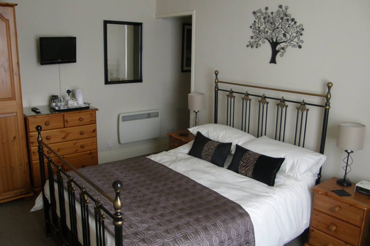 A bedroom with a bed, dresser, nightstand, and a wall-mounted TV.