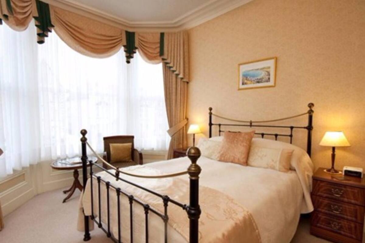 A bedroom with a four-poster bed, a chair, a nightstand, and a window with curtains.