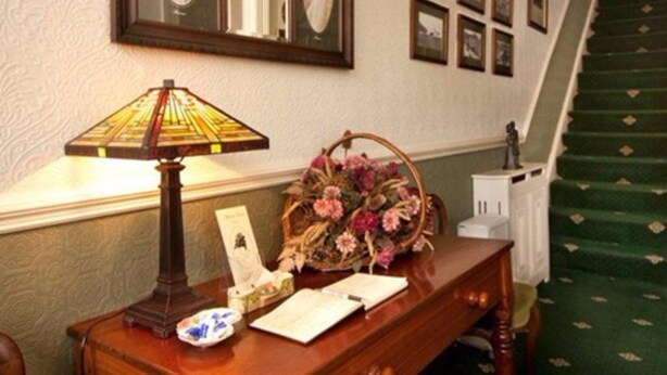 A wooden desk with a stained glass lamp, a vase of flowers, and framed pictures on the wall. - Adcote House (Llandudno)