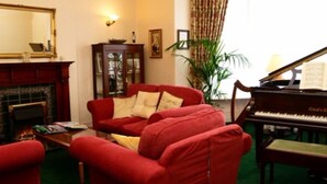 A living room with a red sofa, a piano, a fireplace, and a large mirror. - Adcote House (Llandudno)