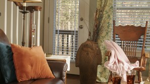 A living room with a brown leather sofa, a wooden coffee table with a book and glasses, and a dining table with a plate of grapes and a glass of iced tea. - Seven Oaks Bed & Breakfast (High Point)