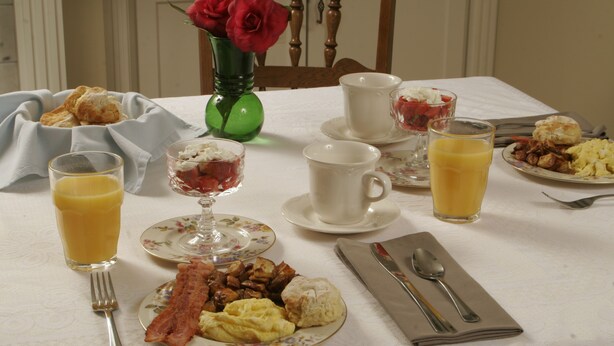 A breakfast table with plates of food, glasses of orange juice, and a vase with red roses. - Seven Oaks Bed & Breakfast (High Point)