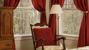 A bedroom with a wooden dresser, a chair with a red pillow, and a lamp. - Seven Oaks Bed & Breakfast (High Point)