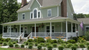 A two-story house with a front porch, a chimney, and a flag. - Seven Oaks Bed & Breakfast (High Point)
