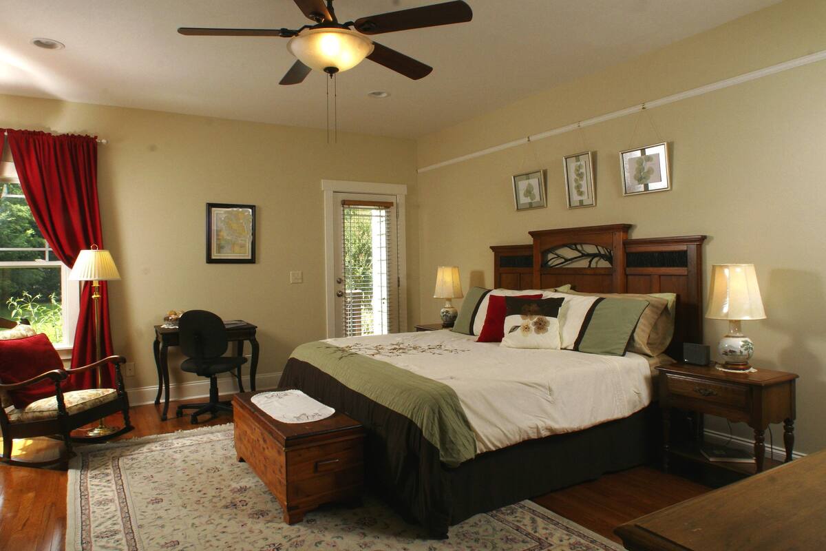 A bedroom with a bed, a desk, a chair, a ceiling fan, and a window with curtains.