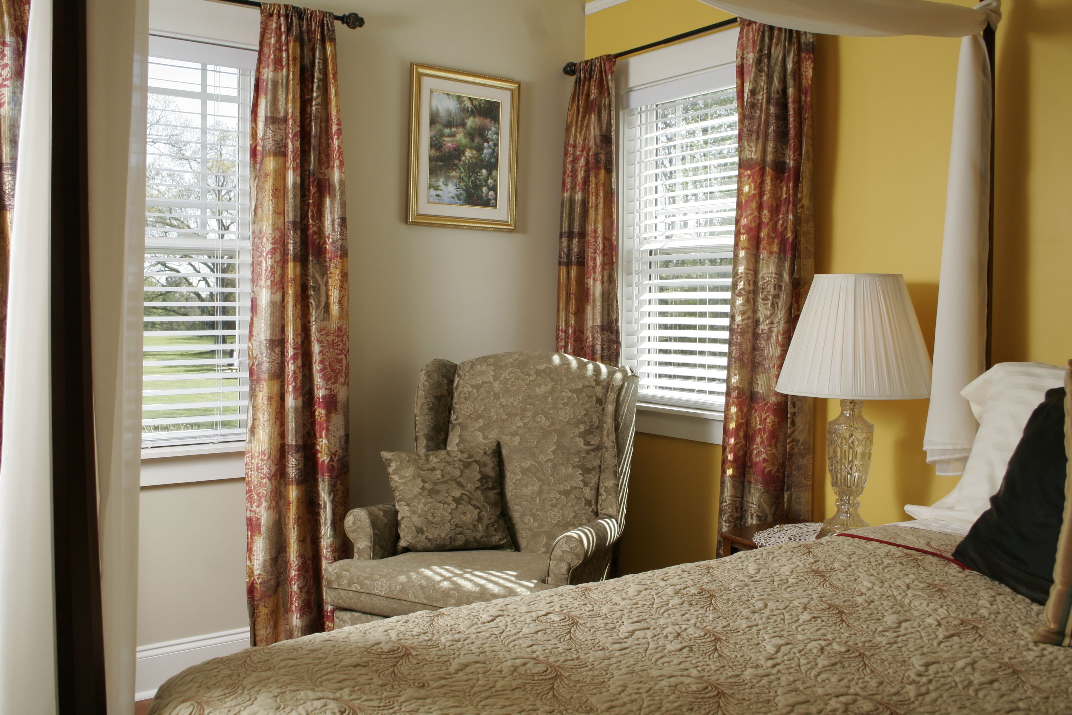 A bedroom with a bed, a chair, a lamp, and curtains.