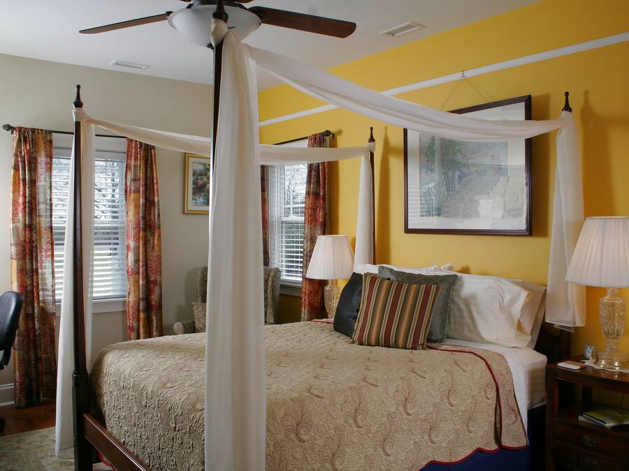 A four-poster bed with a canopy, a desk with a chair, and two bedside lamps.