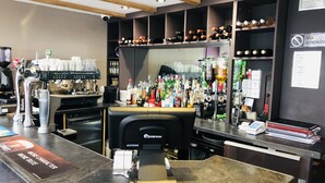 Zona de bar con una máquina de café, estantes llenos de botellas y un cartel de prohibido fumar.