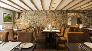 Un restaurante con pared de piedra, vigas de madera en el techo y una larga mesa de comedor con sillas.