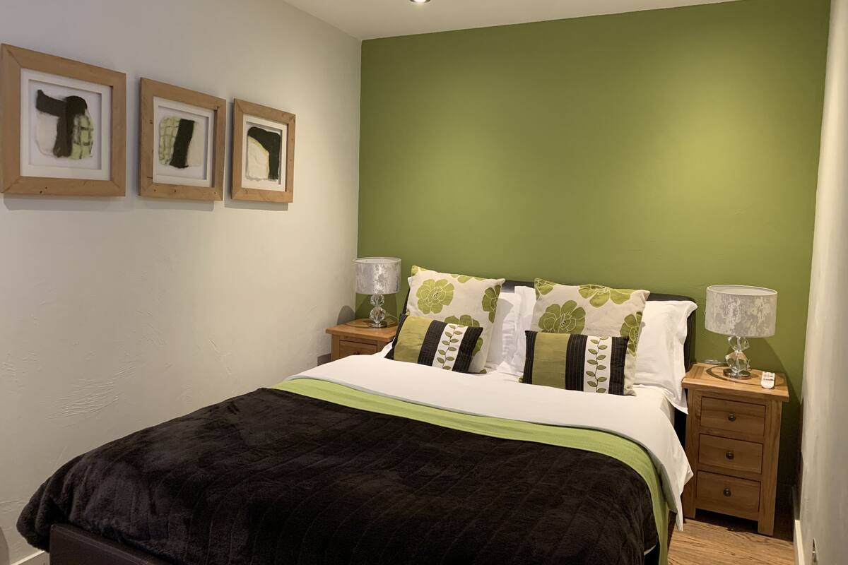 A bedroom with a bed, green walls, and three framed pictures on the wall.