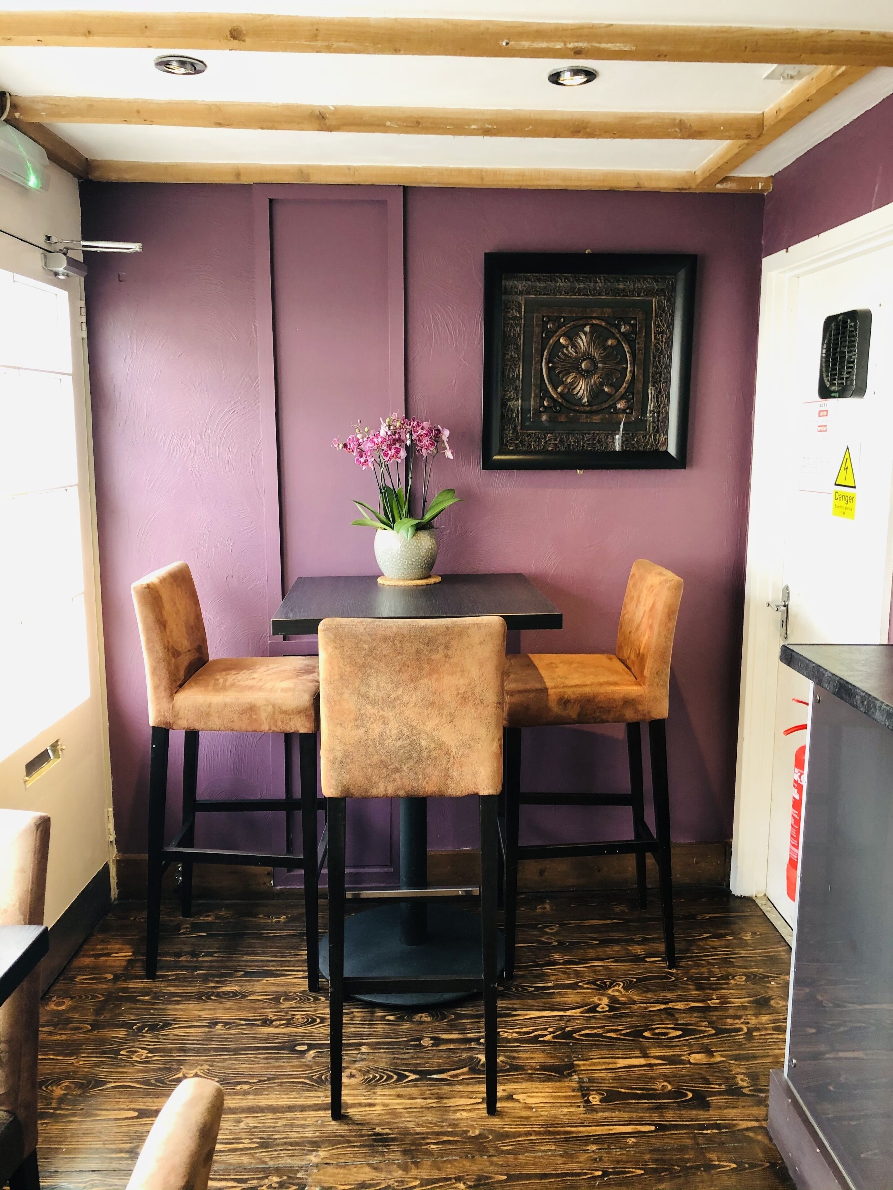 Un comedor con una mesa y cuatro sillas, un florero con flores, una obra de arte enmarcada en la pared y piso de madera.