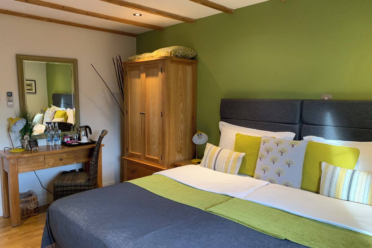 A bedroom with a bed, a wooden wardrobe, a desk with a mirror, and a green wall.