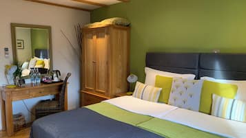 A bedroom with a bed, a wooden wardrobe, a desk with a mirror, and a green wall.