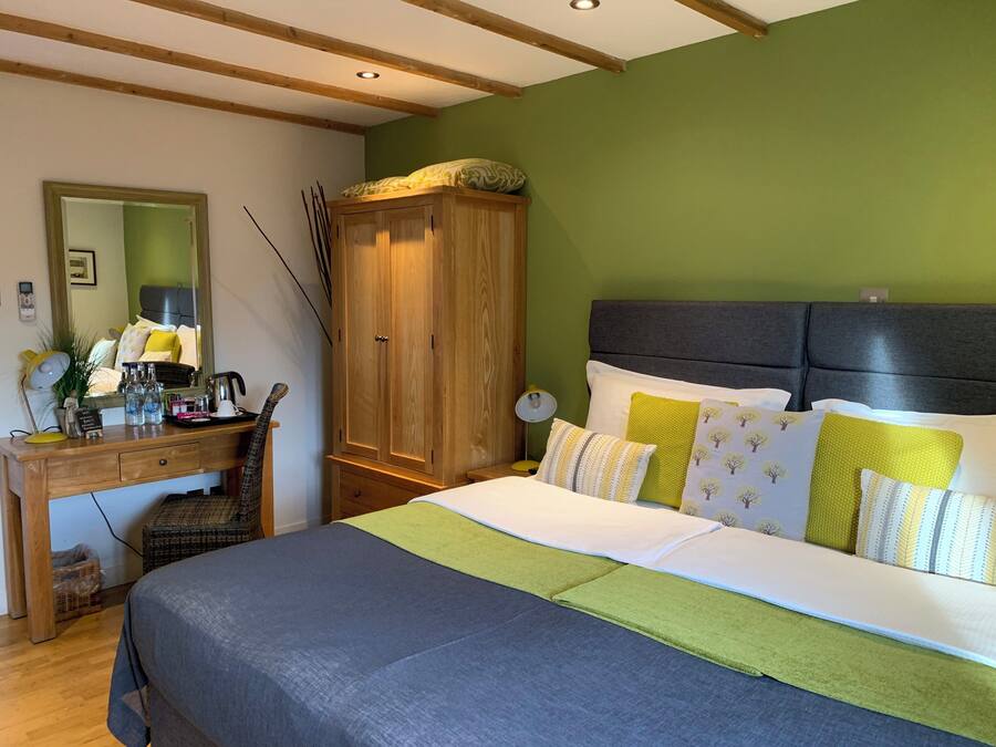 A bedroom with a bed, a wooden wardrobe, a desk with a mirror, and a green wall.