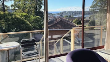 A balcony with a chair, a table, and a view of a residential area with houses and trees.