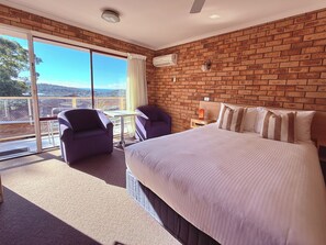 Una habitación de hotel con una cama grande, dos sillones, una mesita, una mesita de noche y vistas a través de un ventanal.