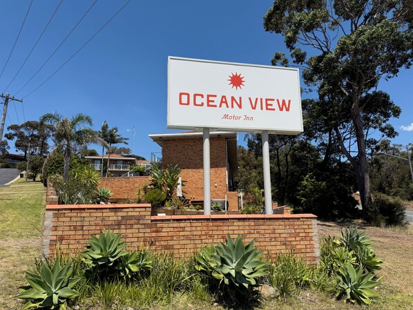 A sign for 'Ocean View Motor Inn' with a brick wall and plants in front.