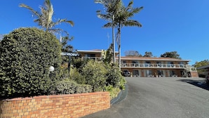 A two-story building with a 'VACANCY' sign, surrounded by well-maintained greenery and a brick wall. - Ocean View Motor Inn (Merimbula)