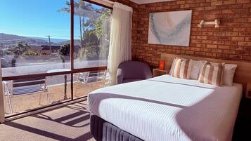 A hotel room with a large bed, a view through a sliding glass door, a brick wall, and a painting on the wall.